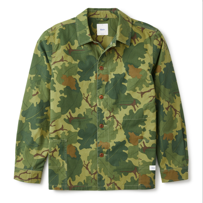 Katin Task Coast in Camo โ flat lay front view of a relaxed cotton chore coat in woodland camo print with a spread collar, brown button front closure, two lower patch pockets, contrast stitching, and a woven label at the hem, on a white background