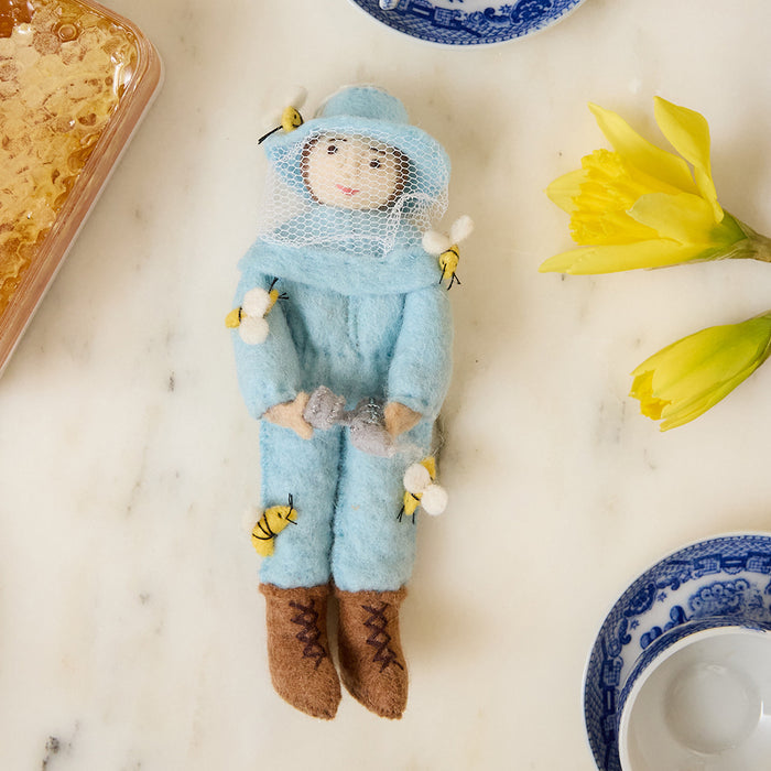 Hand-felted blue beekeeper ornament with brown hair, supporting pollinator awareness