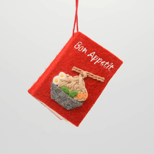 Miniature felt ornament shaped like a cookbook, hand-felted and embroidered with cooking-themed details including salt, pepper, vegetables, and a stovetop. Crafted from merino-blend wool with soft pages and a hanging string, this ornament measures approximately 2.5 inches tall. A cozy tribute to home cooking and culinary tradition. GIF 360 degree book