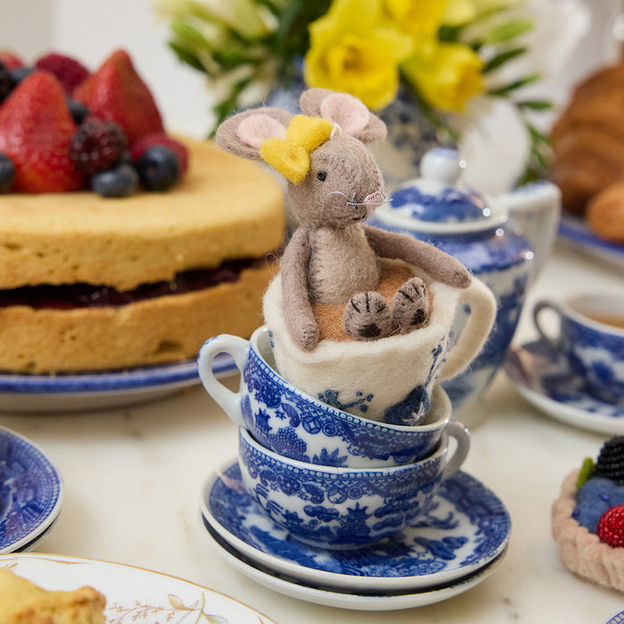 Hand-felted wool ornament of a small gray mouse with a bow, sitting inside a floral teacup with embroidered details. Crafted from merino-blend wool, this whimsical piece evokes tea time and childhood storytelling. Includes a hanging string and measures approximately 4.5 inches tall. A sweet and cozy decoration for tea lovers and mouse enthusiasts alike.