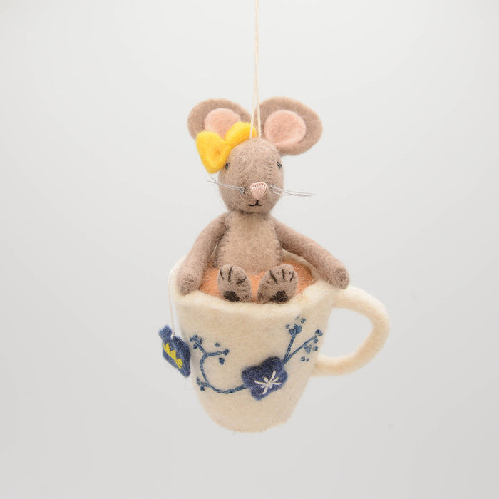 Hand-felted wool ornament of a small gray mouse with a bow, sitting inside a floral teacup with embroidered details. Crafted from merino-blend wool, this whimsical piece evokes tea time and childhood storytelling. Includes a hanging string and measures approximately 4.5 inches tall. A sweet and cozy decoration for tea lovers and mouse enthusiasts alike.