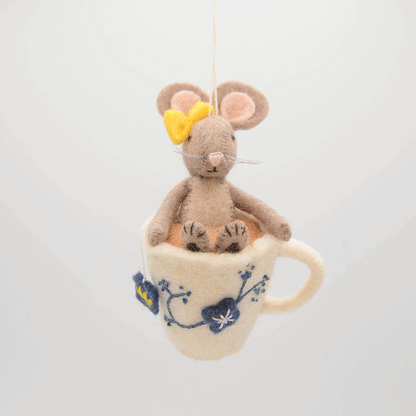 Hand-felted wool ornament of a small gray mouse with a bow, sitting inside a floral teacup with embroidered details. Crafted from merino-blend wool, this whimsical piece evokes tea time and childhood storytelling. Includes a hanging string and measures approximately 4.5 inches tall. A sweet and cozy decoration for tea lovers and mouse enthusiasts alike. GIF 360 degree view.