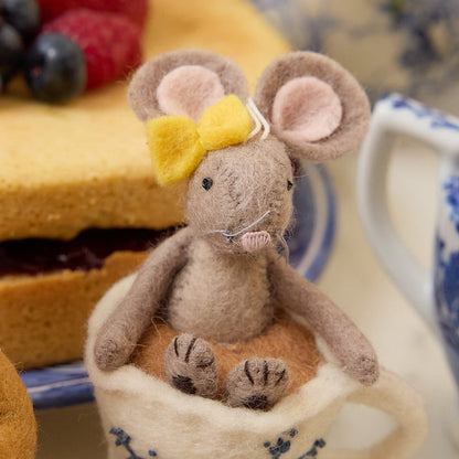 Hand-felted wool ornament of a small gray mouse with a bow, sitting inside a floral teacup with embroidered details. Crafted from merino-blend wool, this whimsical piece evokes tea time and childhood storytelling. Includes a hanging string and measures approximately 4.5 inches tall. A sweet and cozy decoration for tea lovers and mouse enthusiasts alike.