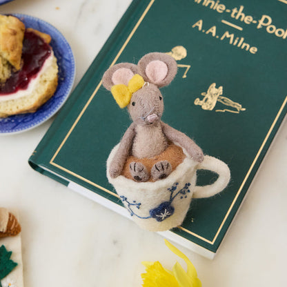 Hand-felted wool ornament of a small gray mouse with a bow, sitting inside a floral teacup with embroidered details. Crafted from merino-blend wool, this whimsical piece evokes tea time and childhood storytelling. Includes a hanging string and measures approximately 4.5 inches tall. A sweet and cozy decoration for tea lovers and mouse enthusiasts alike.