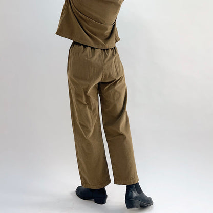 Back and side view of the Bryn Walker Corduroy Pleated Pants in Partridge, showing elastic back waistband, straight leg, full-length hem, and olive pinwheel corduroy drape, styled with matching jacket and black Chelsea boots