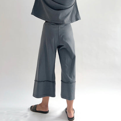 Back view of model wearing Pacific Cotton dolomite crop full pant, showing elastic waistband, wide flared leg, layered hem panel with exposed seam detail, and washed slate grey color, styled with matching dolomite boxy shirt