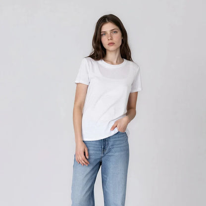 Model wearing It Is Well Everyday Crewneck Tee in Salt, full front view against light grey background showing crisp white lightweight slub jersey, crew neck, short sleeves with slight cuff, and relaxed full-length fit, styled with light wash wide-leg jeans and taupe Birkenstock slide sandals, hand in pocket