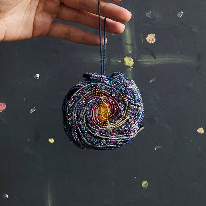 Beaded galaxy Christmas ornament featuring spiral Milky Way design with detailed embroidery. Handmade satin decoration for stargazers and space lovers.