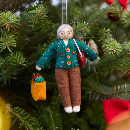 Handmade felt Grandma ornament from Craftspring, wearing a cozy beaded and embroidered holiday sweater, holding a designer purse and a shopping bag full of presents—displayed on a Christmas tree, evoking warm holiday memories and timeless festive cheer, ethically crafted by artisans using sustainable wool.