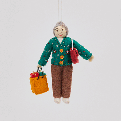 Handmade felt Grandma ornament from Craftspring rotating to show front, side, and back views—featuring detailed beadwork and embroidery on a holiday sweater, a designer purse, and a shopping bag full of presents, showcasing heirloom craftsmanship, ethically crafted by artisans using sustainable wool.