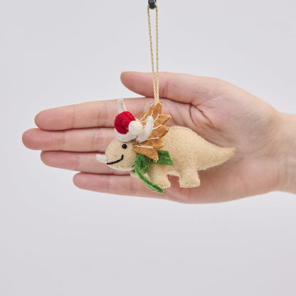 Handmade felt Santa Triceratops ornament from Craftspring held in front of a hand to show size—featuring embroidered and beaded details, a red Santa hat, and a green scarf, showcasing artisan craftsmanship and festive holiday charm, ethically crafted using sustainable wool.