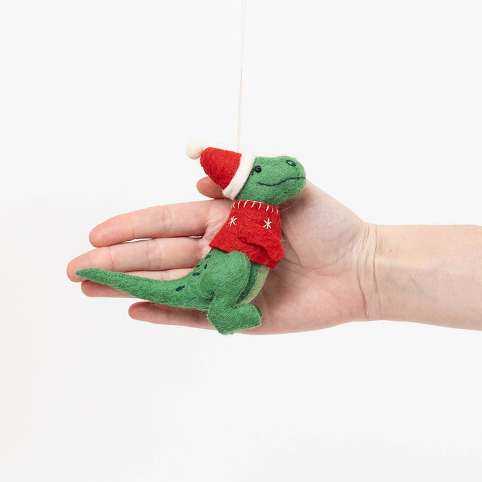 Handmade felt Santasaurus T-Rex ornament from Craftspring held in front of a hand to show size—featuring a red Santa hat, red sweater, and embroidered details, perfect for dino-loving kids and festive holiday gifting, ethically crafted using sustainable wool.