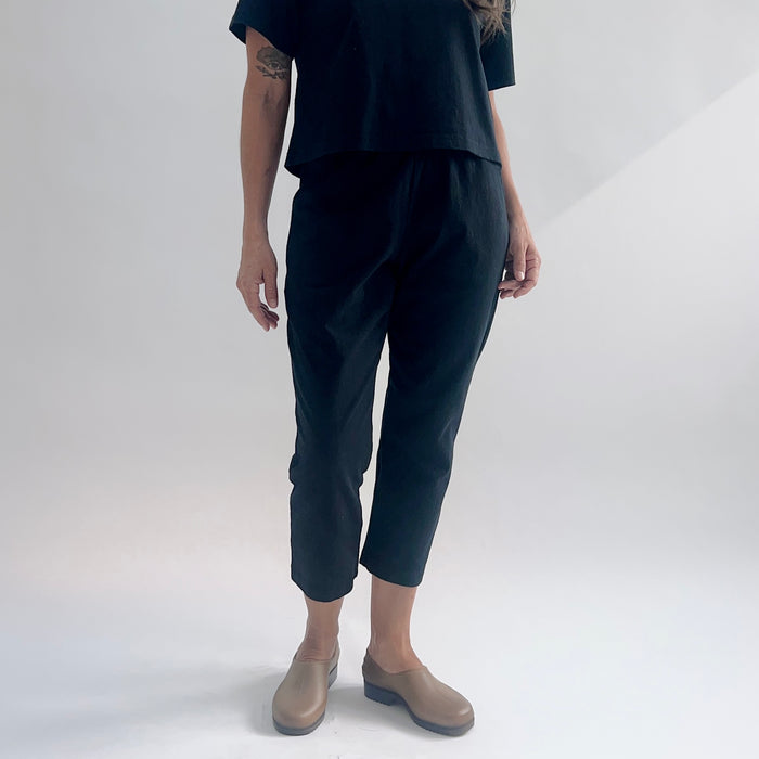 Front view of model wearing black cropped Sunday pants with a relaxed fit, paired with a black boxy tee and tan loafers against a white background.